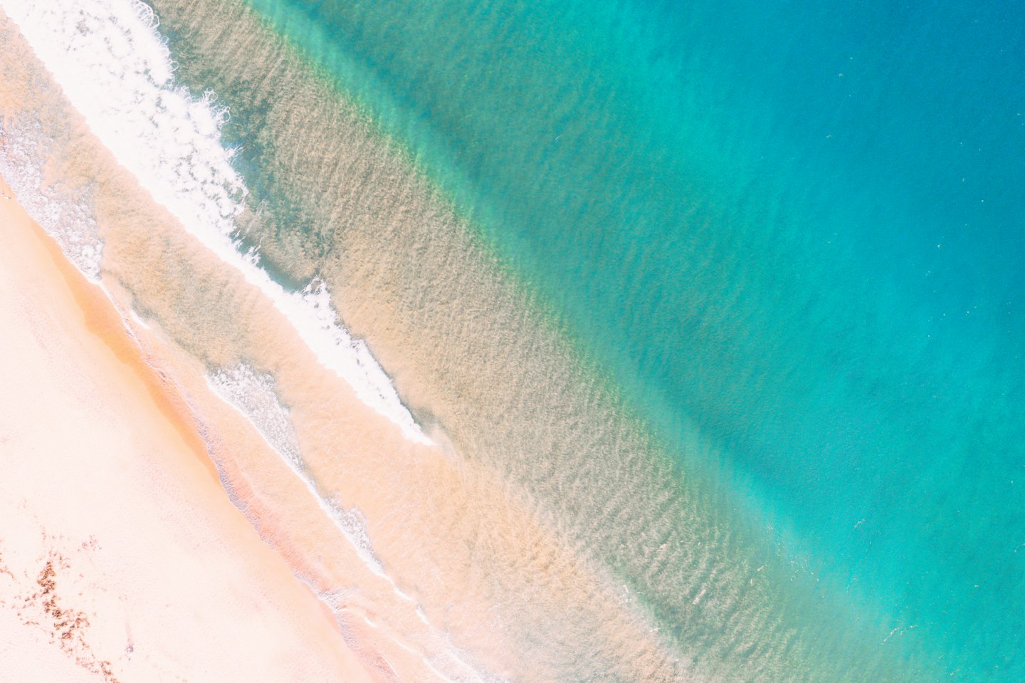 Luftaufnahme von türkisfarbenem Meerwasser, das auf einen Sandstrand trifft.