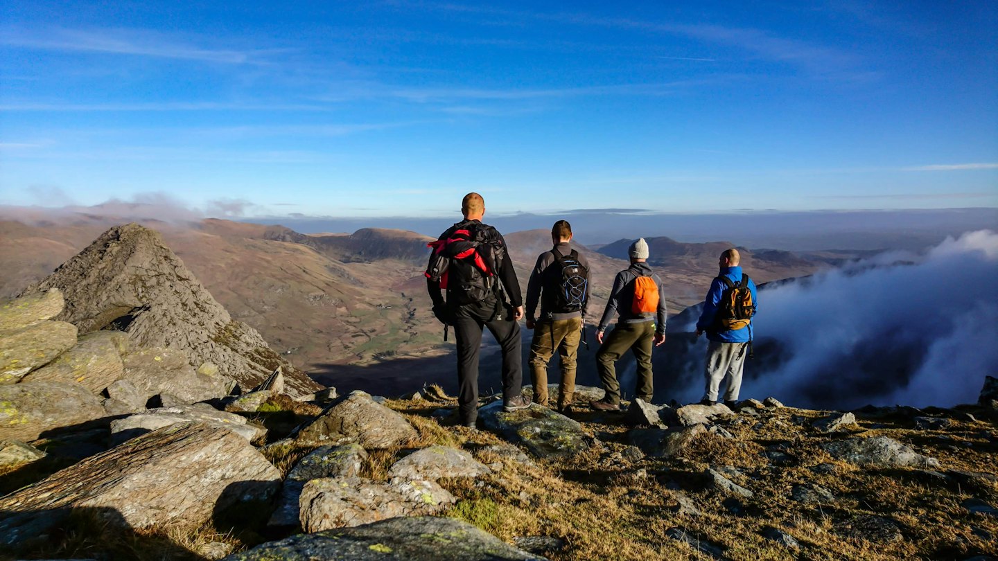 Vier Rucksacktouristen stehen auf einem felsigen Berggipfel mit Blick auf Täler.
